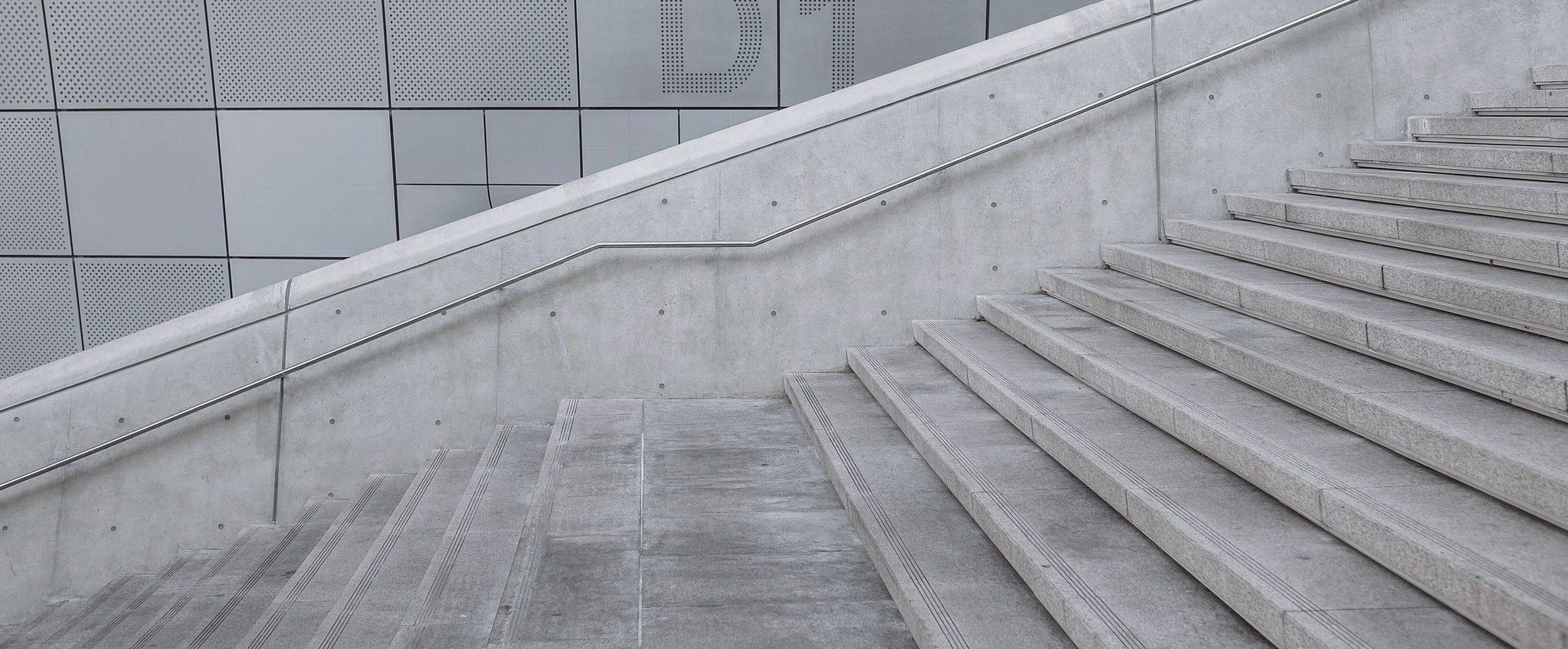 Escalera y rampa de hormigón visto junto a un muro de paneles